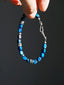 Ocean Wing bracelet suspended by its blue beads, with silver spacers and the curved fishhook clasp visible
