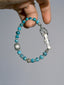 Sun Seeker turquoise and silver bracelet held between fingers, showing the eagle clasp and flower-shaped accent.