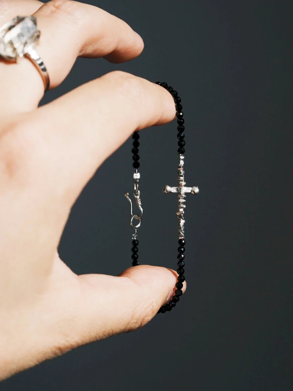 A hand holds the Silver Ronin bracelet, showing black faceted beads, silver spacers, a central silver detail and a hook clasp.
