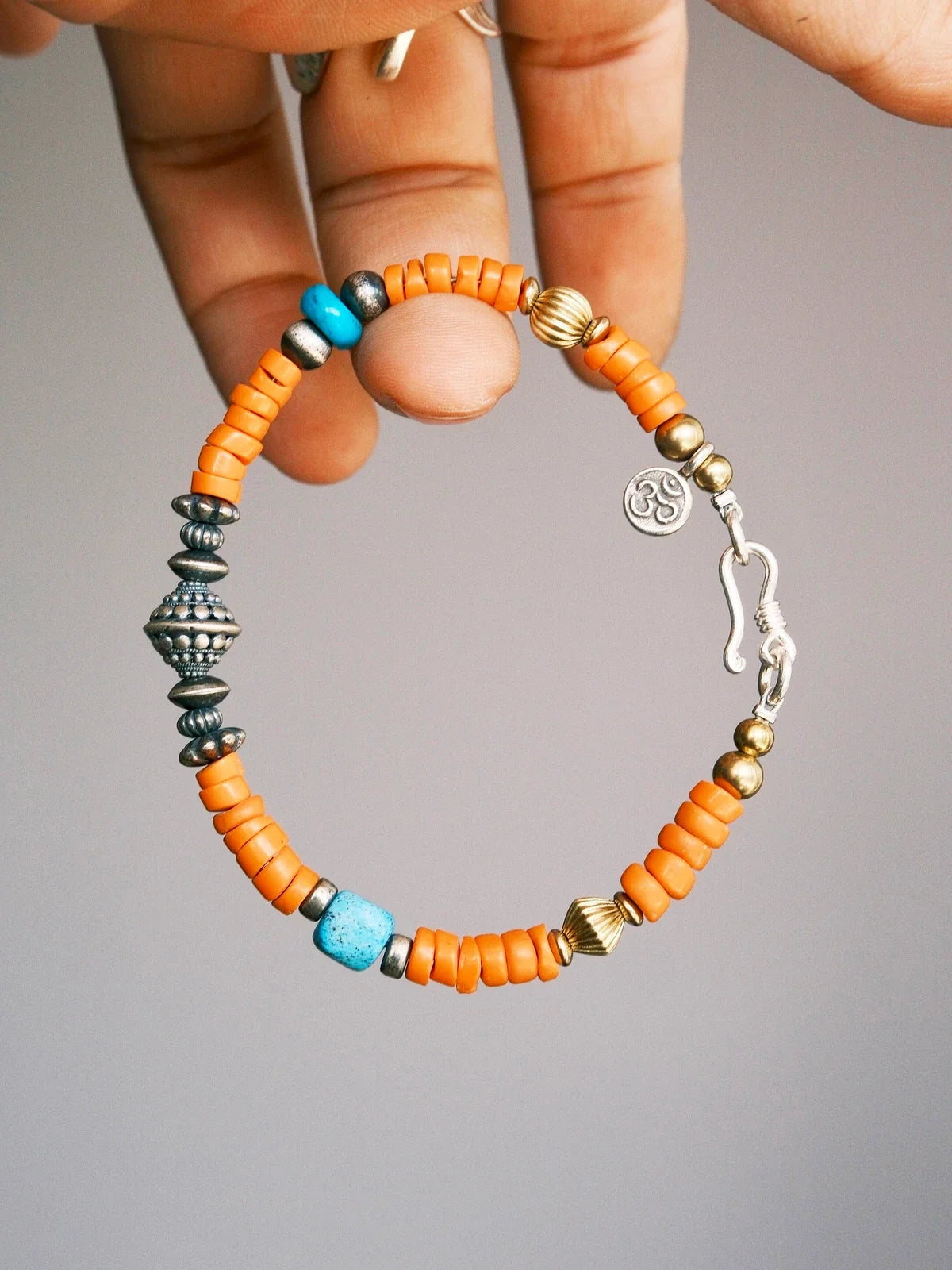 Hand holding Sunset Nomad, with orange Miyuki colored-glaze, turquoise, 925 silver components, a fishhook clasp and brass accents.