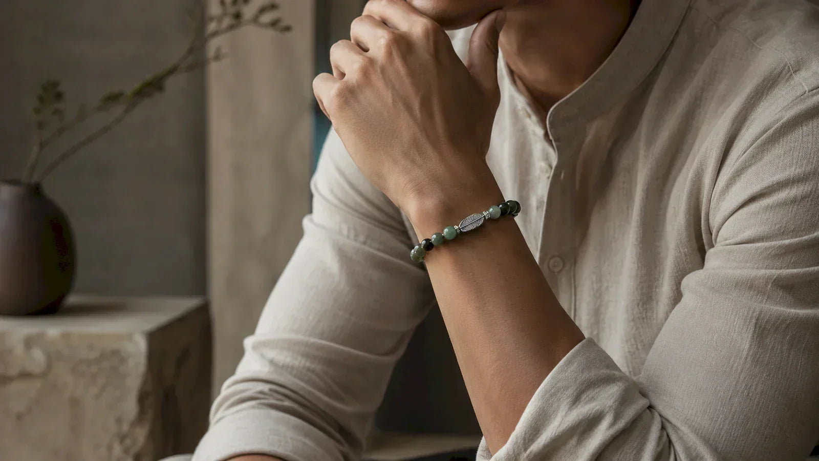 Man in a light linen shirt wearing a green beaded bracelet with a silver-colored feather detail.