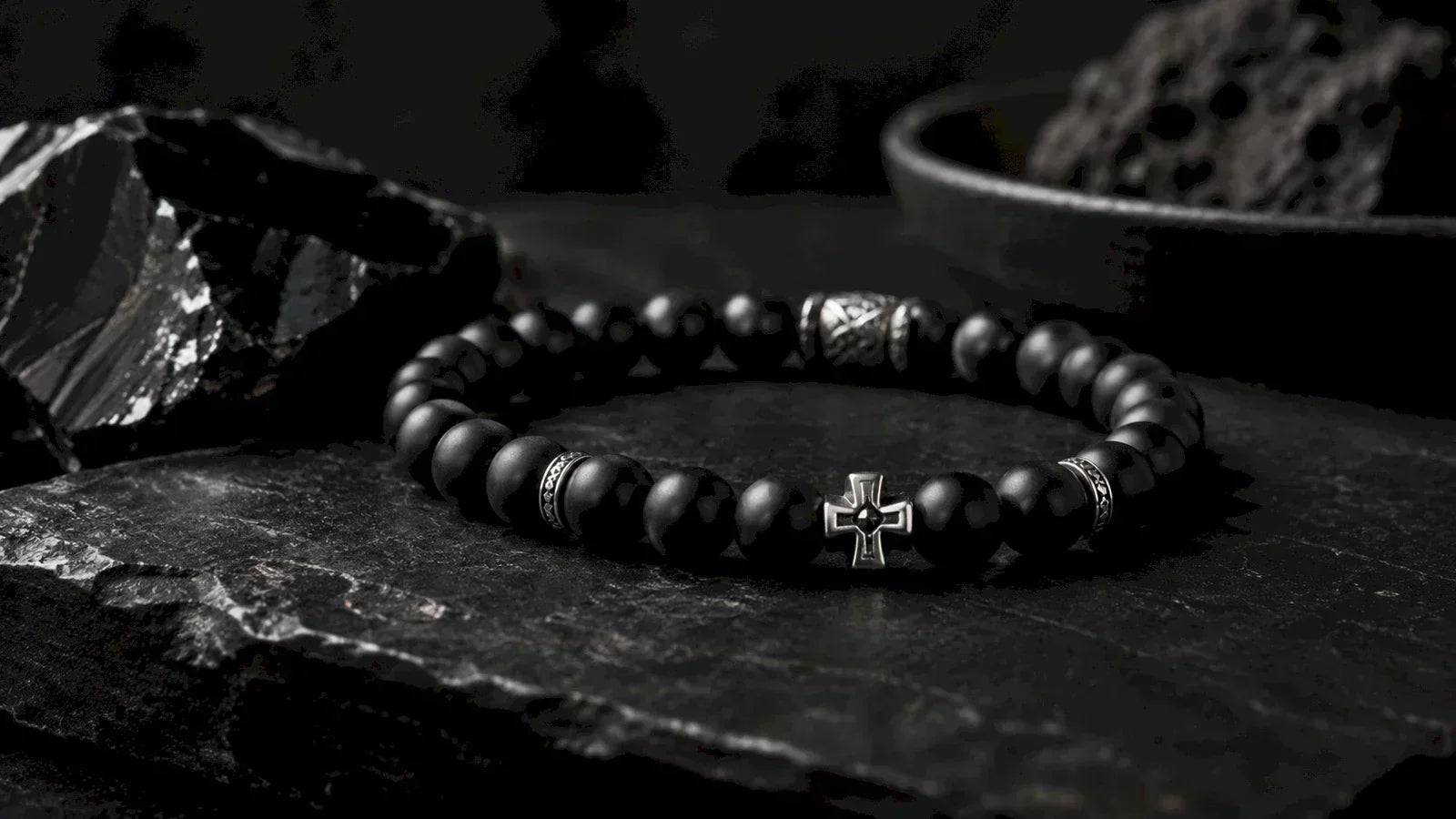 Matte black beaded bracelet with a silver-colored cross and patterned accents on dark stone.