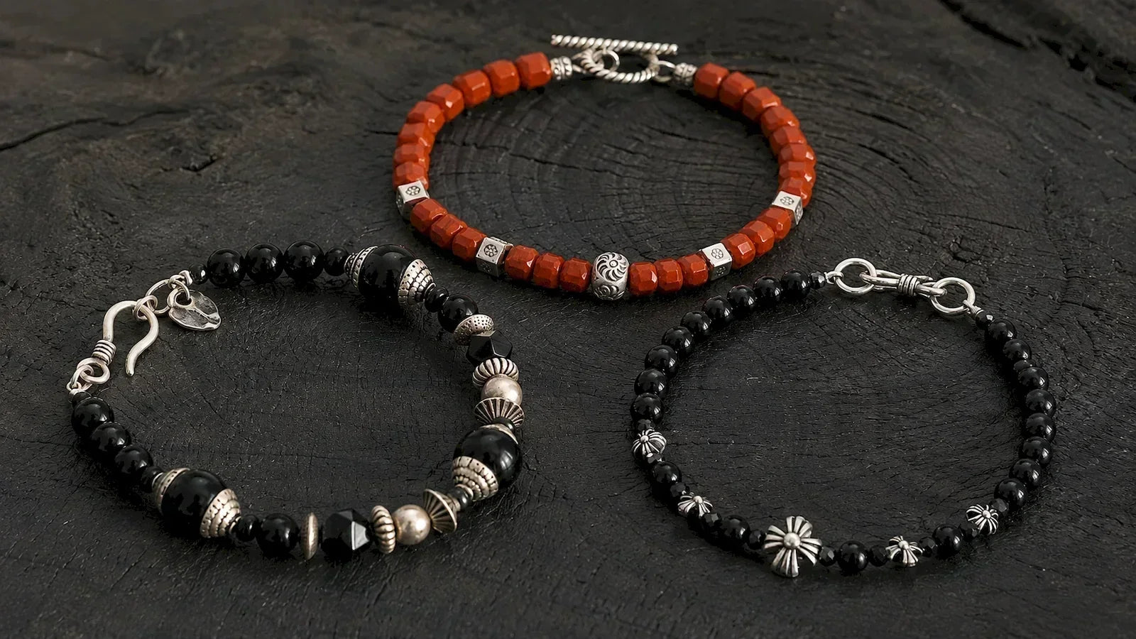 Red agate, black onyx and black obsidian bracelets for men with silver details on a dark textured surface.