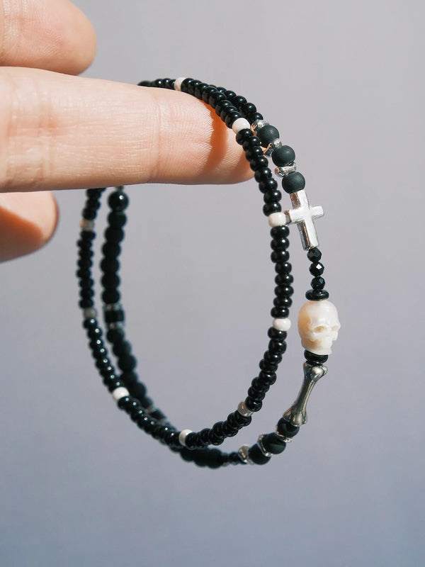 Close up hand holding double wrap black beaded bracelet with skull charm and silver cross detail