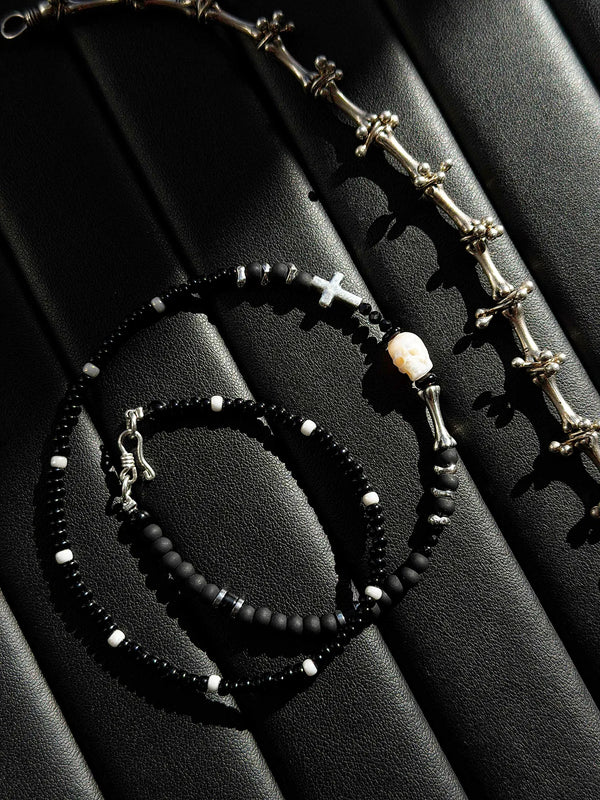 Artistic presentation of handmade black bead bracelet with skull and cross symbolic jewelry design