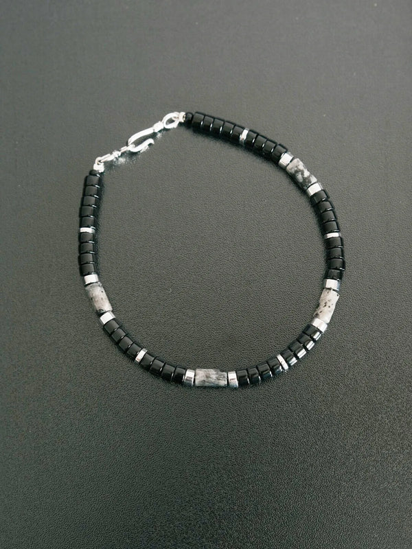 Flat lay of men’s black obsidian beaded bracelet with silver accents on dark textured surface