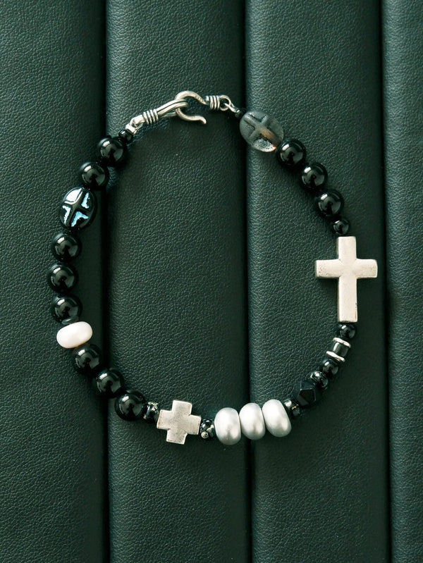 Black and white mood image of minimalist men’s bracelet with black obsidian pearl and silver cross