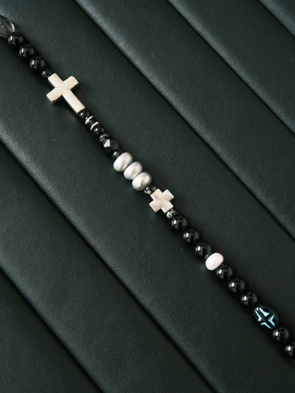 Close-up detail of black obsidian beads, grey pearl, white pearl and silver cross bracelet for men