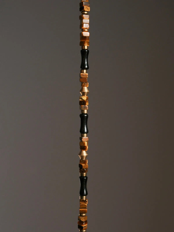 Artistic display of a black gold men’s bracelet with tiger eye, obsidian and brass in sculptural composition