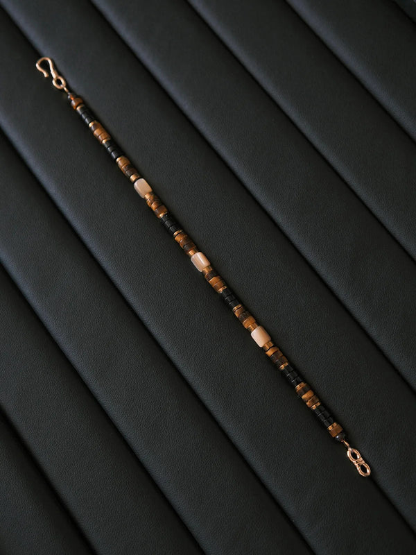Flat lay of Silent Authority tiger eye and black onyx men’s bracelet on black leather with gold shell accents