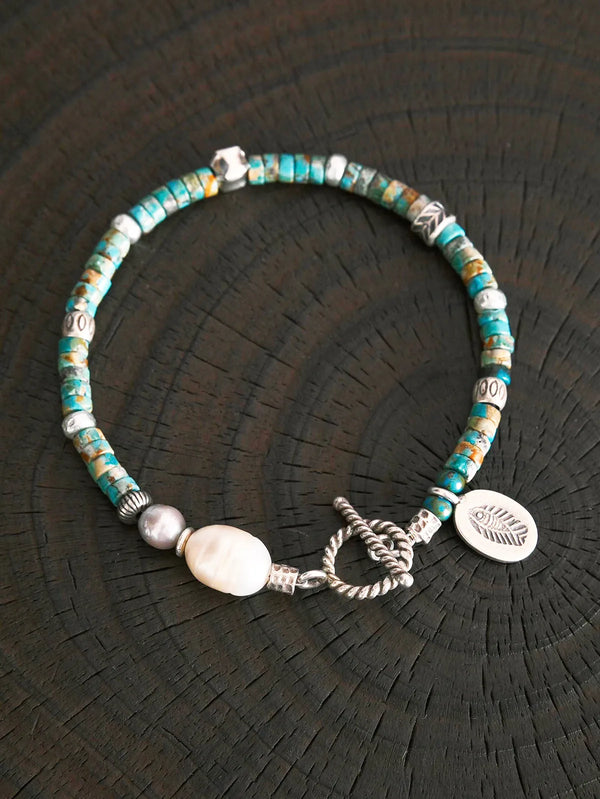 Men’s turquoise pearl bracelet with sterling silver charm, displayed on black tray for luxury product detail