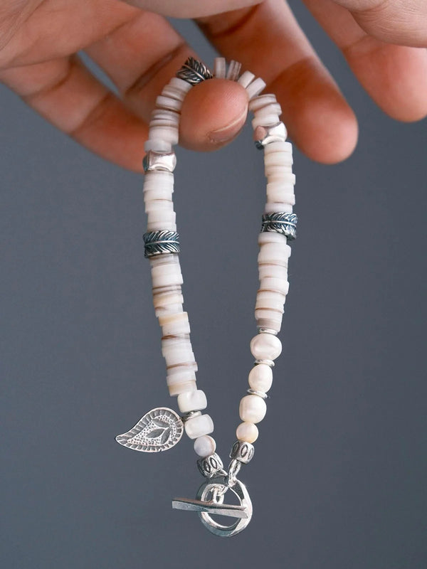 Hand holding men’s shell pearl bracelet with sterling silver feather charm, close-up product view