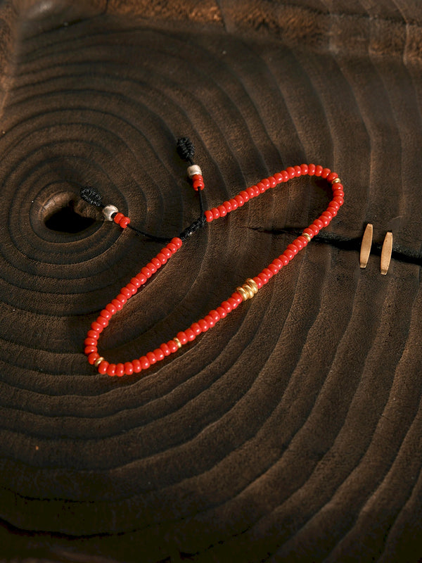 Flat lay of a red colored-glaze men’s bracelet with gold accents on dark textured background, minimal identity jewelry style