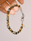 Hand holding a tiger eye men’s bracelet with sterling silver feather charm, close-up product angle, refined natural stone jewelry.