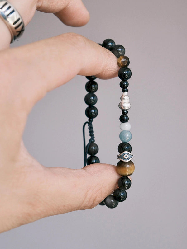 Hand holding a men’s obsidian tiger eye bracelet, Mineral Soul Series Obsidian Hawk, showing black stone beads, silver gourd detail, jade accent, and refined minimal style.