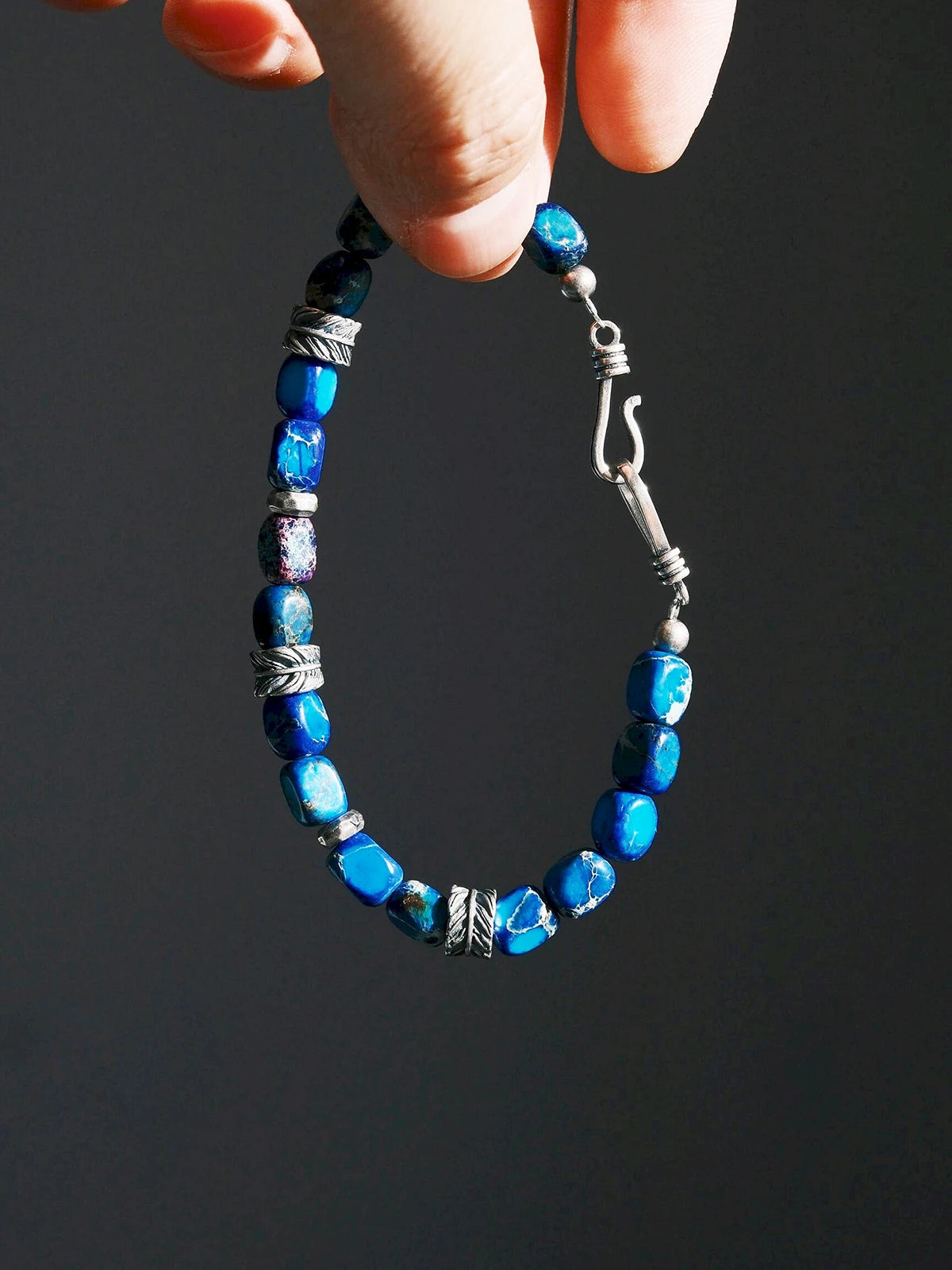 Ocean Wing bracelet suspended by its blue beads, with silver spacers and the curved fishhook clasp visible Main image