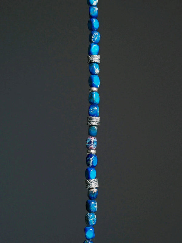 Close-up of blue jasper-style stone beads and sterling silver feather details on a men’s beaded bracelet with ocean-inspired texture.