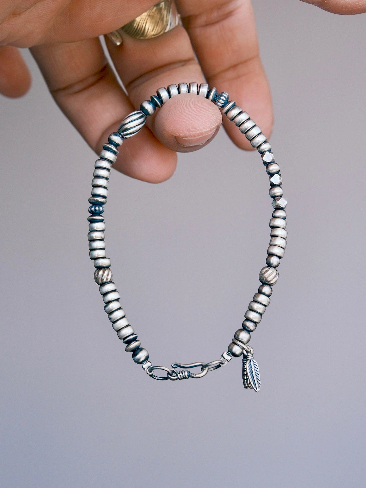 Hand-held close-up of Silver Nomad 925 silver bracelet showing silver bead shapes, hook clasp and feather charms