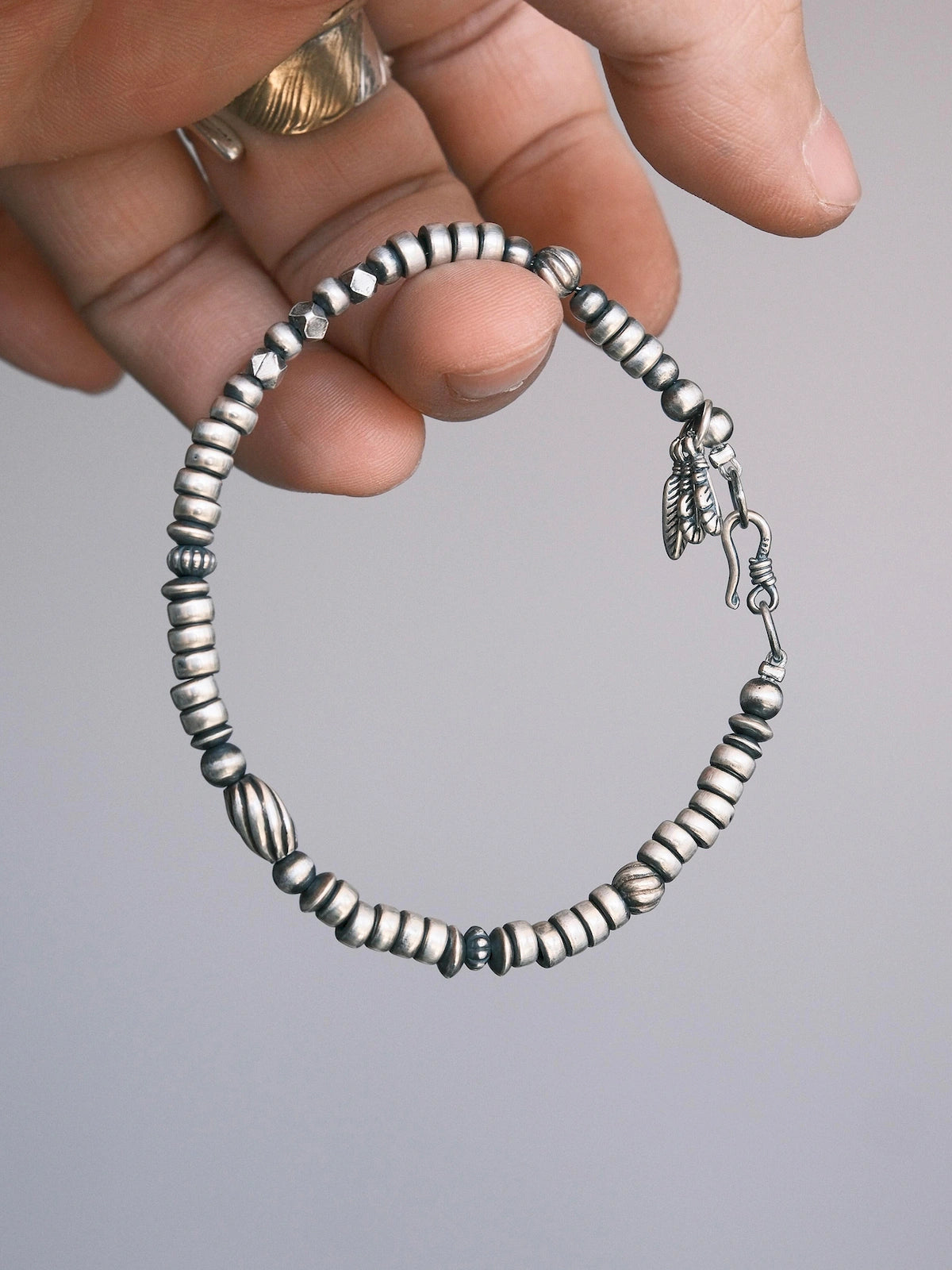 Hand-held close-up of Silver Nomad 925 silver bracelet showing silver bead shapes, hook clasp and feather charms Main image