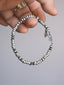Hand-held close-up of Silver Nomad 925 silver bracelet showing silver bead shapes, hook clasp and feather charms