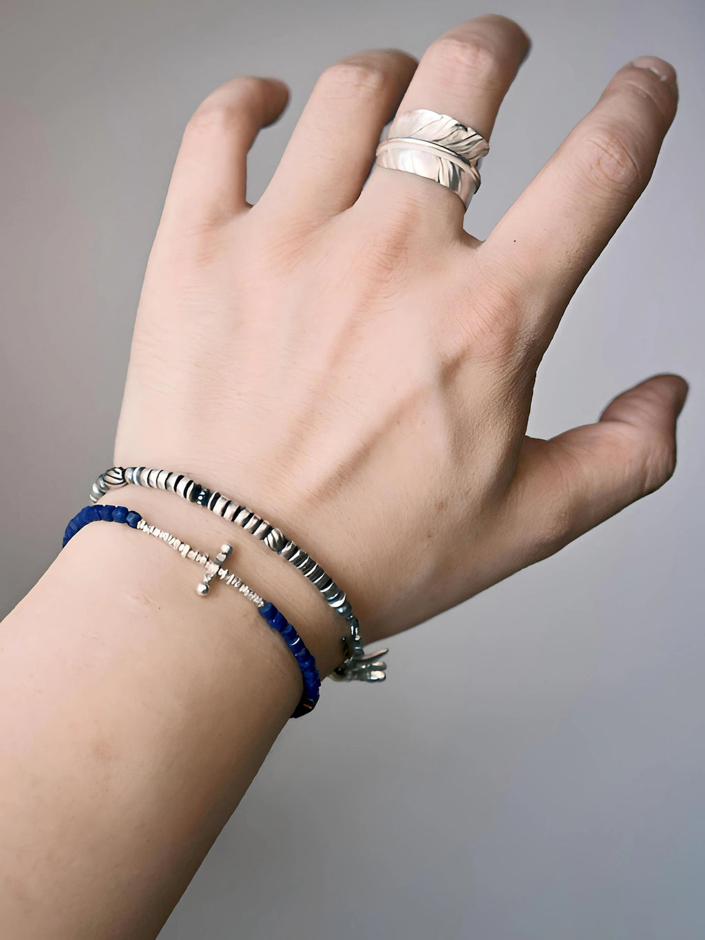 Close wrist view of a sterling silver feather bracelet layered with a blue bracelet, refined men's jewelry styling