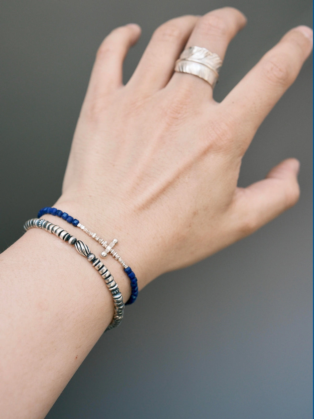 Close wrist view of a sterling silver feather bracelet layered with a blue bracelet, refined men's jewelry styling