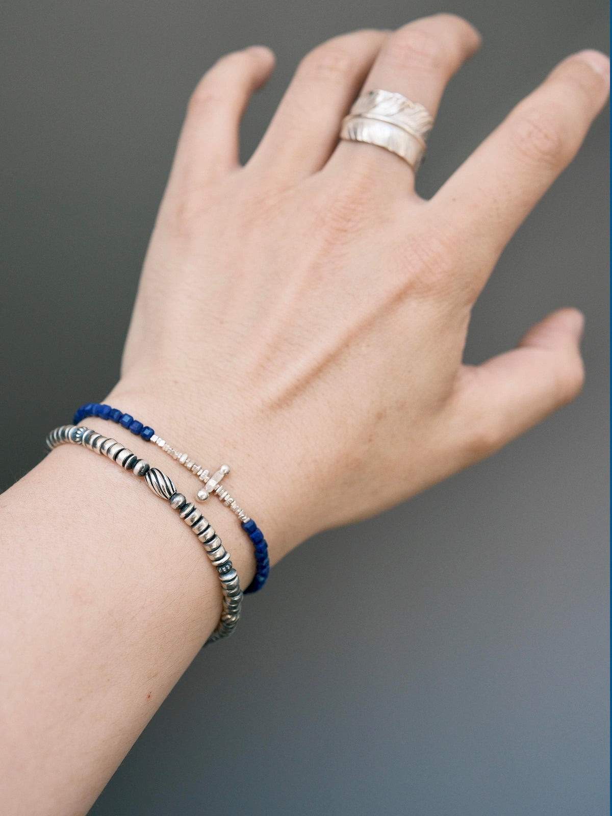 Close wrist view of a sterling silver feather bracelet layered with a blue bracelet, refined men's jewelry styling