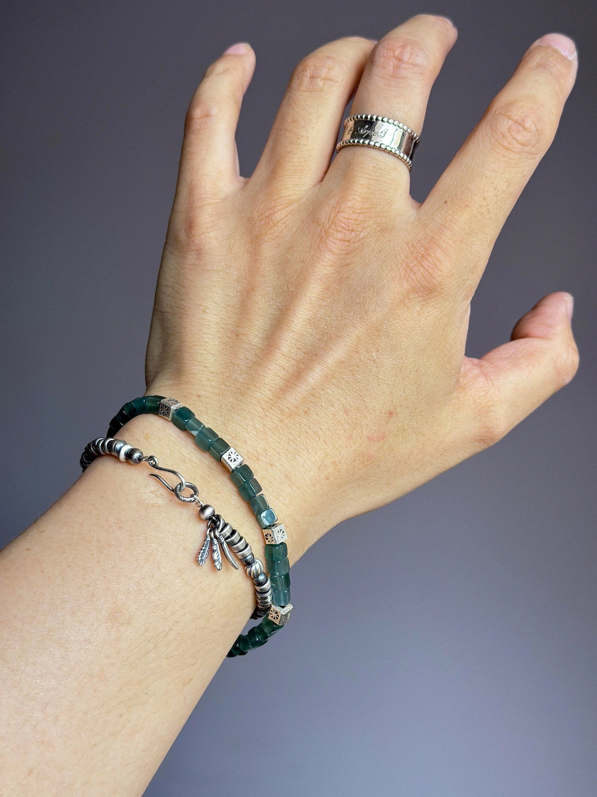 Men's sterling silver feather bracelet stacked with a green stone bracelet on wrist, minimalist everyday jewelry close-up