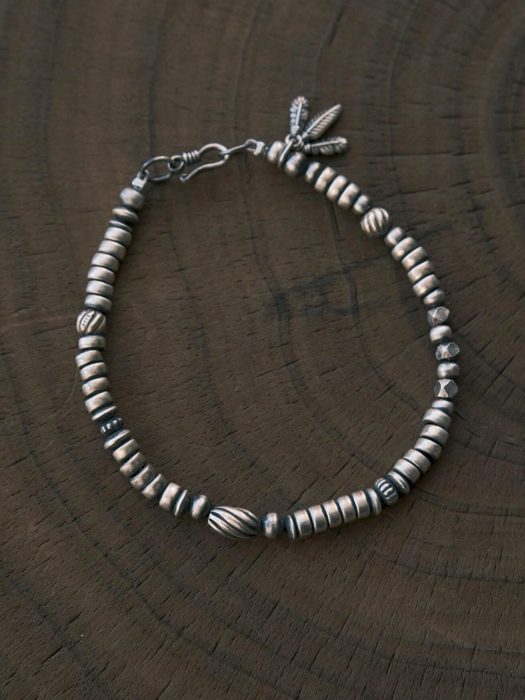 Silver Nomad men's sterling silver feather bracelet laid on carved dark wood, oxidized silver detail flat lay