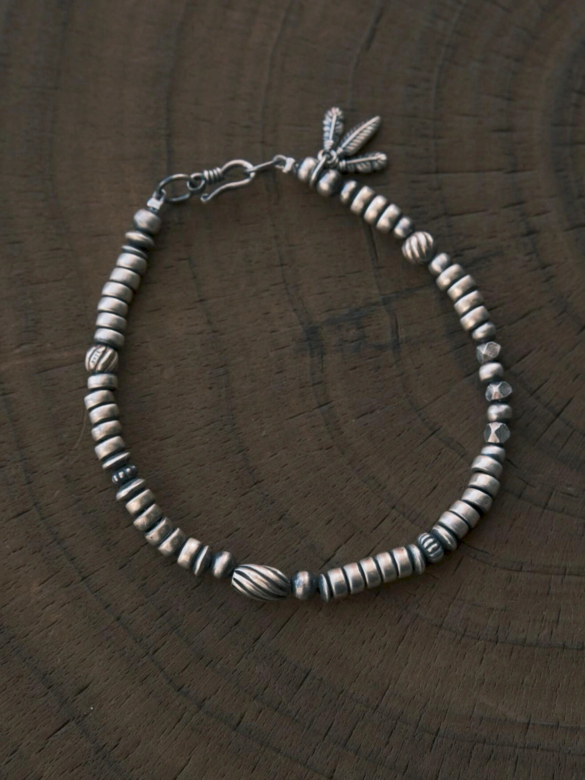 Silver Nomad men's sterling silver feather bracelet laid on carved dark wood, oxidized silver detail flat lay