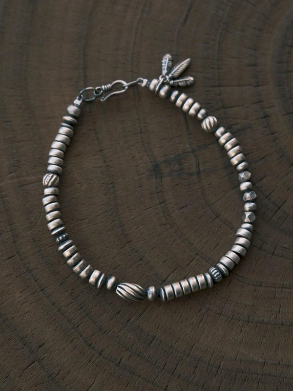 Silver Nomad men's sterling silver feather bracelet laid on carved dark wood, oxidized silver detail flat lay