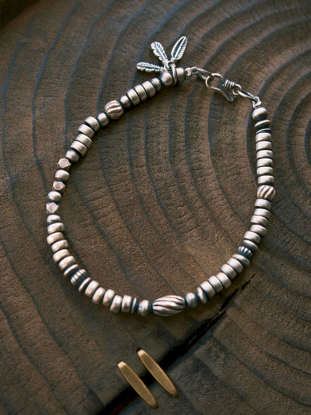 Silver Nomad men's sterling silver feather bracelet laid on carved dark wood, oxidized silver detail flat lay