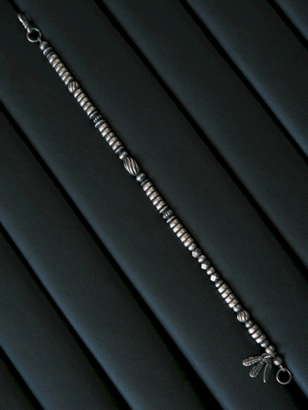 Full-length Silver Nomad sterling silver bracelet laid on black leather, oxidized silver beads and feather charm detail