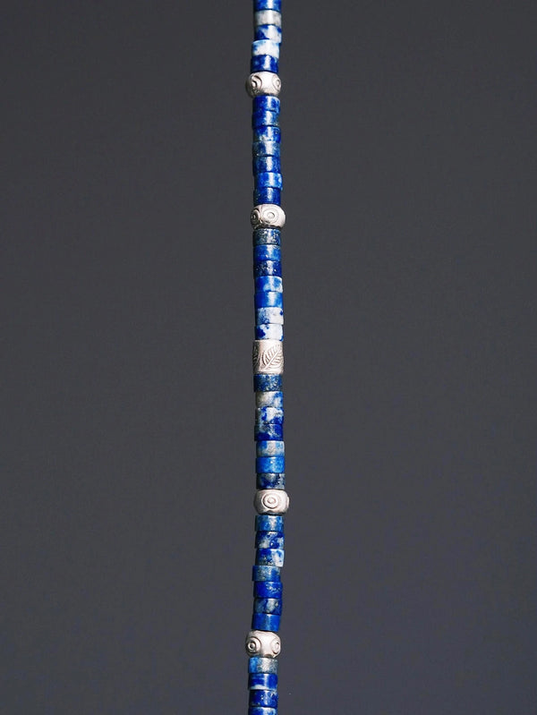Close-up detail of lapis lazuli beads, sterling silver feather charm, hammered silver, and Japanese colored-glaze accents on a men’s bracelet.