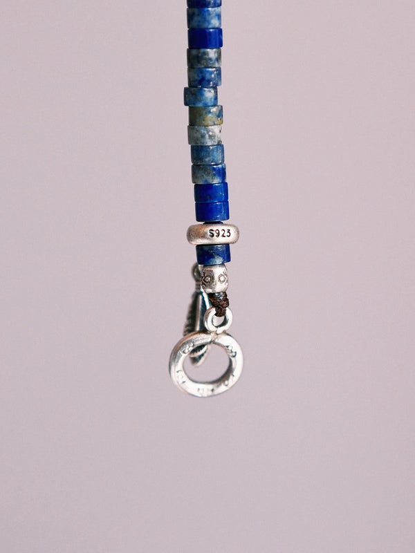 Close-up detail of lapis lazuli beads, sterling silver feather charm, hammered silver, and Japanese colored-glaze accents on a men’s bracelet.