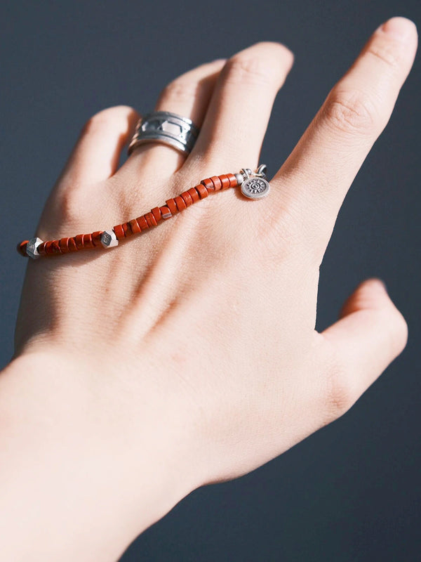 Hand holding a red Bloodstone (Oriental Jasper) beaded bracelet with hammered sterling silver details, close-up product angle, refined men’s jewelry