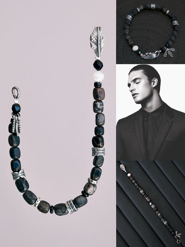 Flat lay of men’s black onyx and sterling silver bracelet with dark imperial jasper-style stone beads, pearl accent, and silver feather details on a dark textured surface.