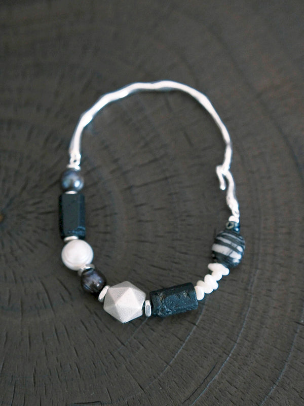 Close-up of silver Mobius ring detail on men’s Urban Stoic bracelet with pearl and raw black tourmaline accents.
