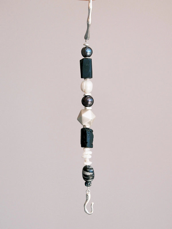 Close-up of black pearl, white pearl, and baroque pearl details on a masculine men’s bracelet with silver and raw stone accents.