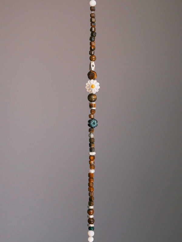 Daisy Youth unisex beaded bracelet laid flat on dark surface, featuring tiger eye, mother-of-pearl daisy, pearl, Czech colored-glaze and silver accents.