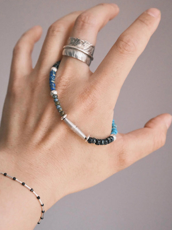 Hand holding Identity Series Cyan Wayfarer bracelet, showing Miyuki colored-glaze beads, sterling silver clasp, and hammered silver texture in a clean product detail angle