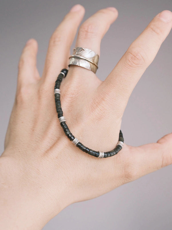 Hand holding a men’s golden obsidian bracelet with hammered silver details, showing the dark mineral beads and refined daily wear aesthetic.