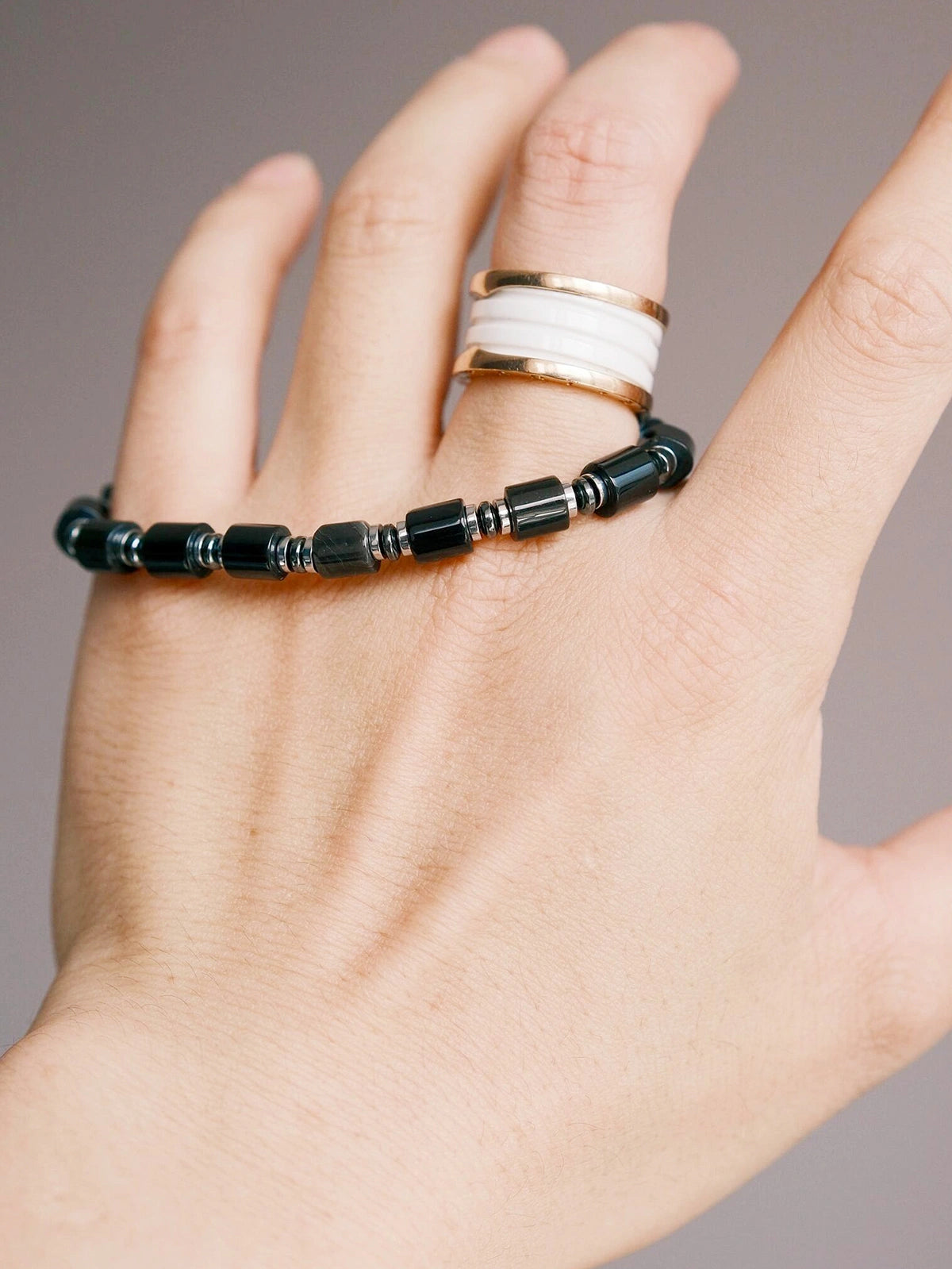 Hand holding a black onyx and hematite men’s bracelet, close-up product view, polished black beads, refined black-silver styling.