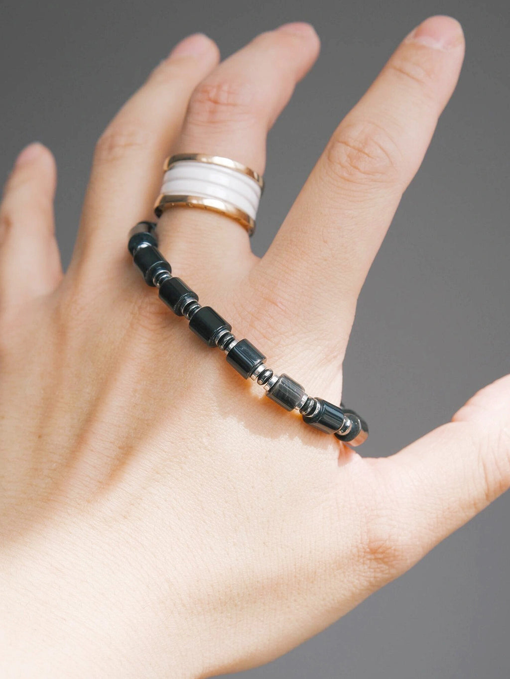Hand holding a black onyx and hematite men’s bracelet, close-up product view, polished black beads, refined black-silver styling.