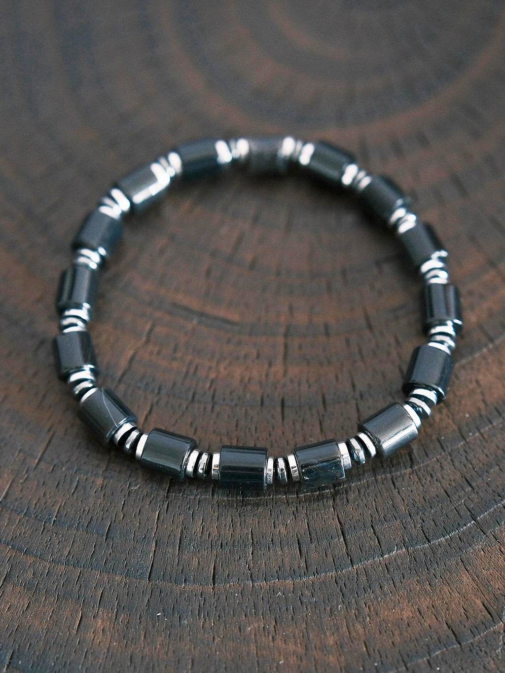 Black onyx and hematite bracelet on dark wood texture, men’s minimal black-silver jewelry, refined product photography.