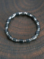 Black onyx and hematite bracelet on dark wood texture, men’s minimal black-silver jewelry, refined product photography.