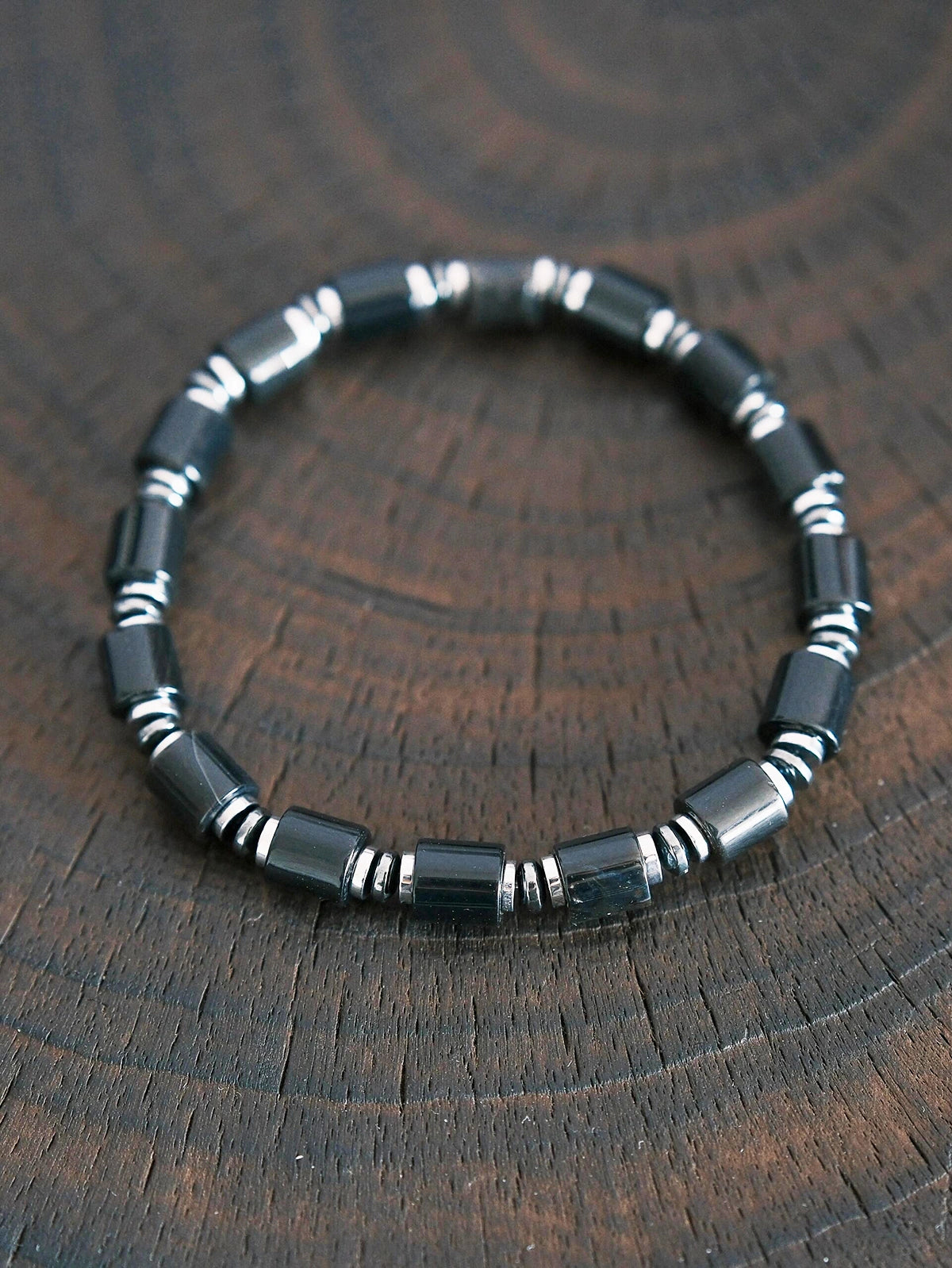 Black onyx and hematite bracelet on dark wood texture, men’s minimal black-silver jewelry, refined product photography.