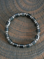 Black onyx and hematite bracelet on dark wood texture, men’s minimal black-silver jewelry, refined product photography.