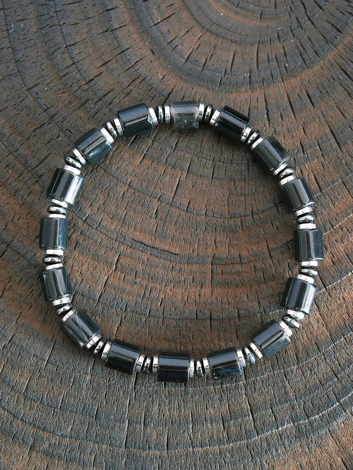 Black onyx and hematite bracelet on dark wood texture, men’s minimal black-silver jewelry, refined product photography.