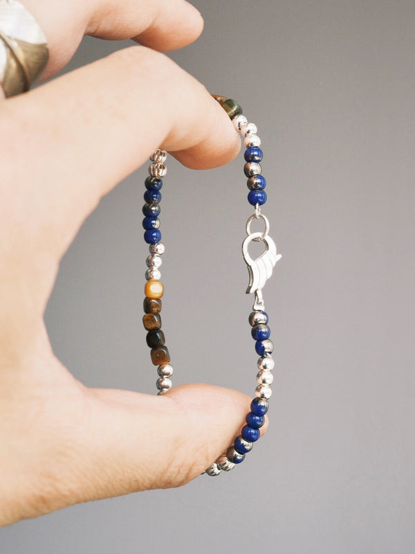 Hand holding Identity Series Silver Epoch men’s bracelet, tiger eye square beads, sterling silver spacers, blue colored-glaze accents.